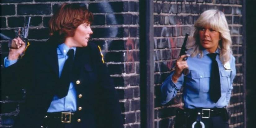 Cagney and Lacey hiding around two corners of a brick wall.