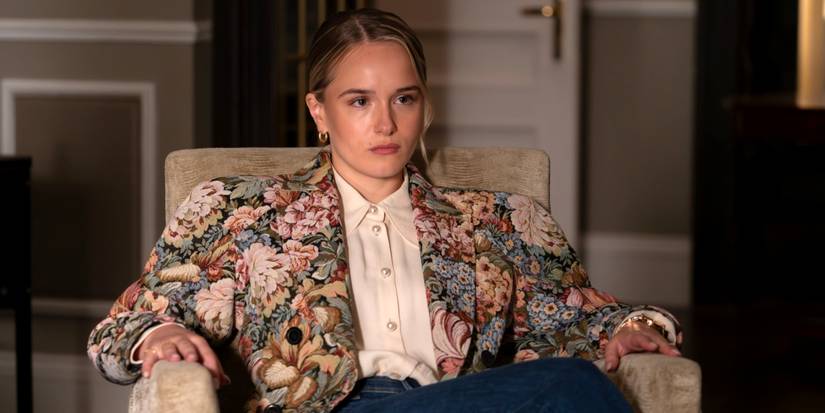 Miriam Petche as Sweetpea Golightly sitting in a chair resting her hands on the arms in Industry Season 4