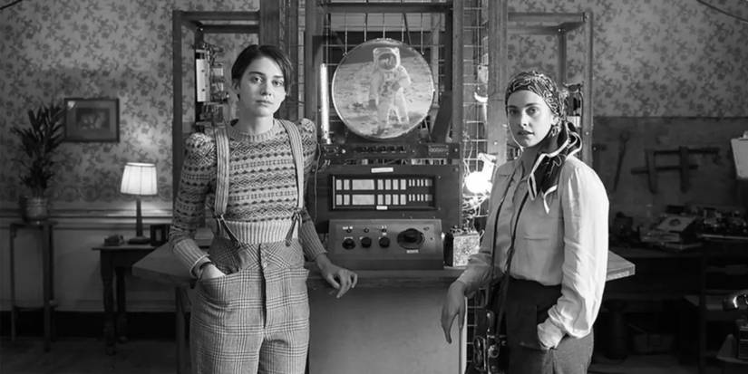 Thom (Emma Appleton) and Mars (Stefanie Martini) stand in front of a machine called LOLA.