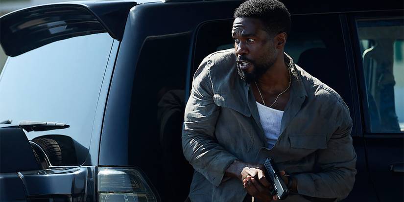 A man with a gun standing by a car in Man on Fire.