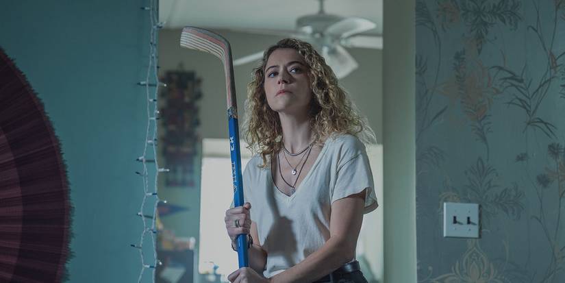 A woman standing by a doorway holding a hockey stick in Maximum Pleasure Guaranteed.