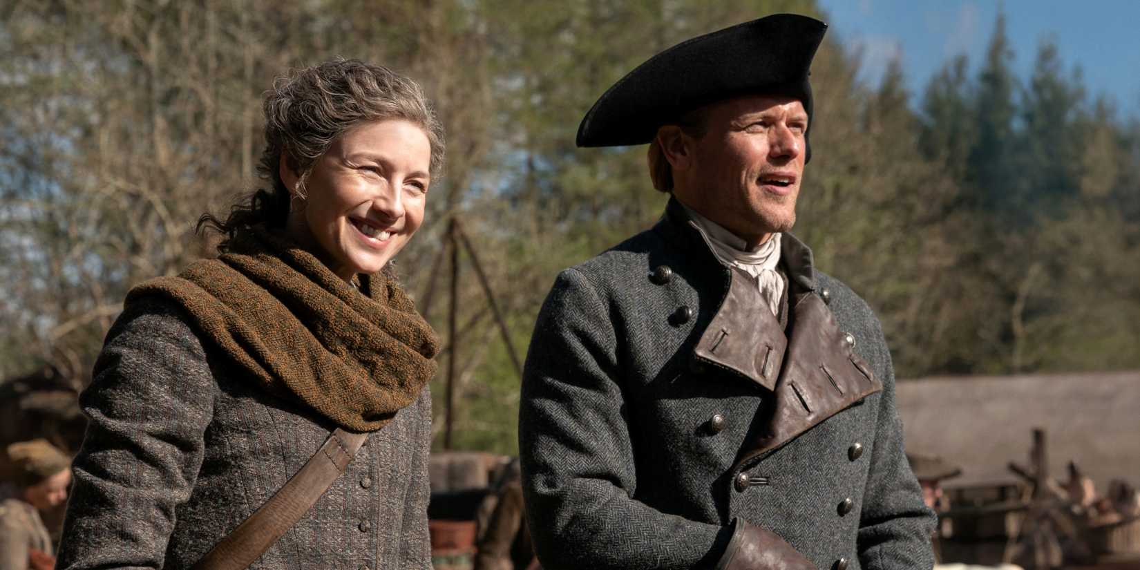 Caitriona Balfe as Claire smiling while standing next to Sam Heughan as Jamie in Outlander Season 8