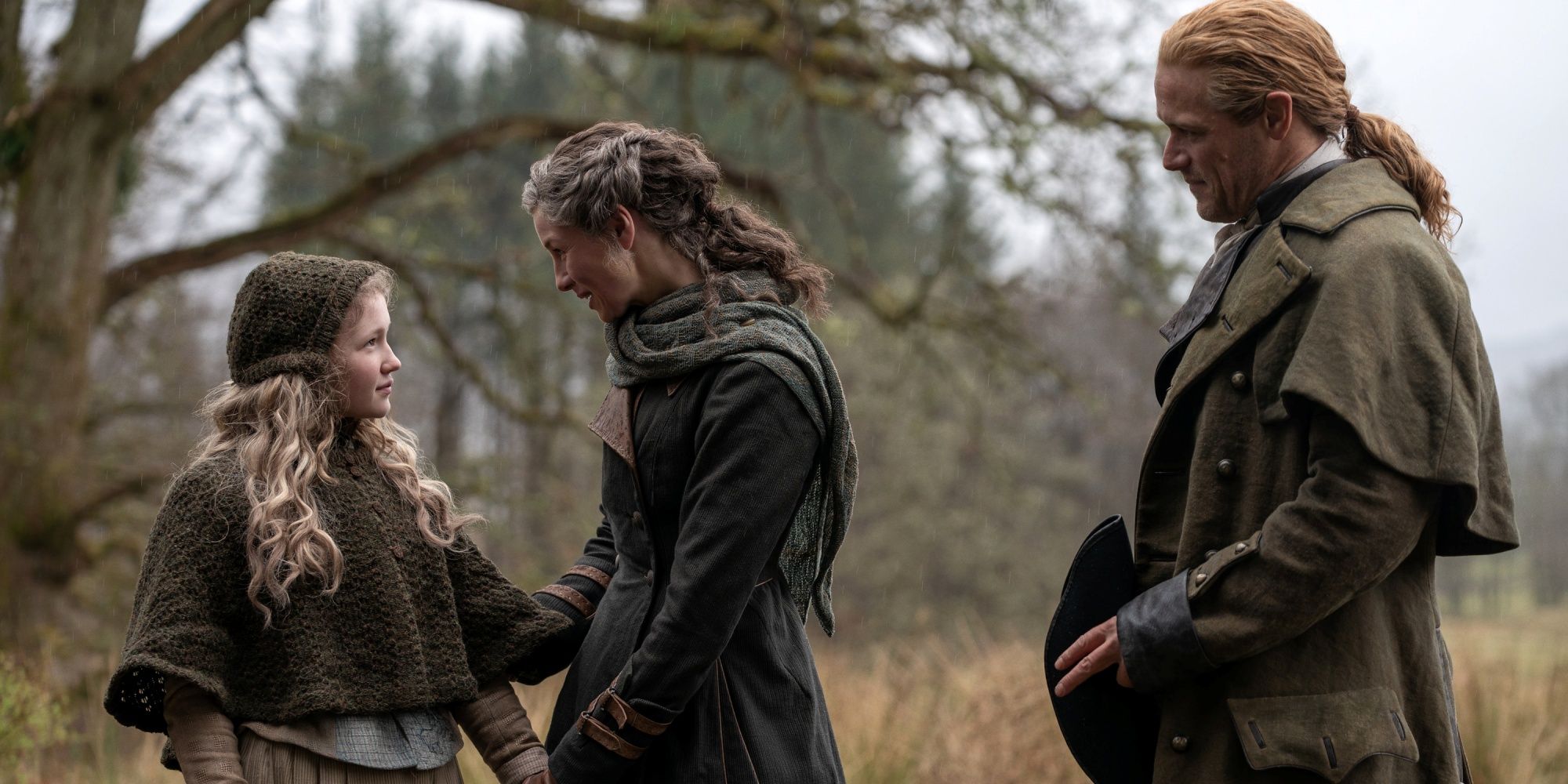 Caitriona Balfe as Claire and Sam Heughan as Jamie standing with Fanny in Outlander Season 8