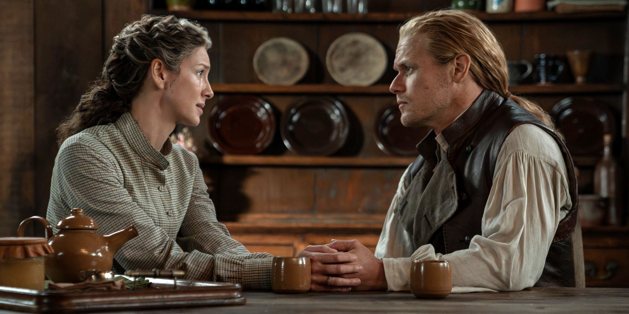 Sam Heughan as Jamie Fraser with Caitriona Balfe as Claire sitting at a table together in Outlander Season 8