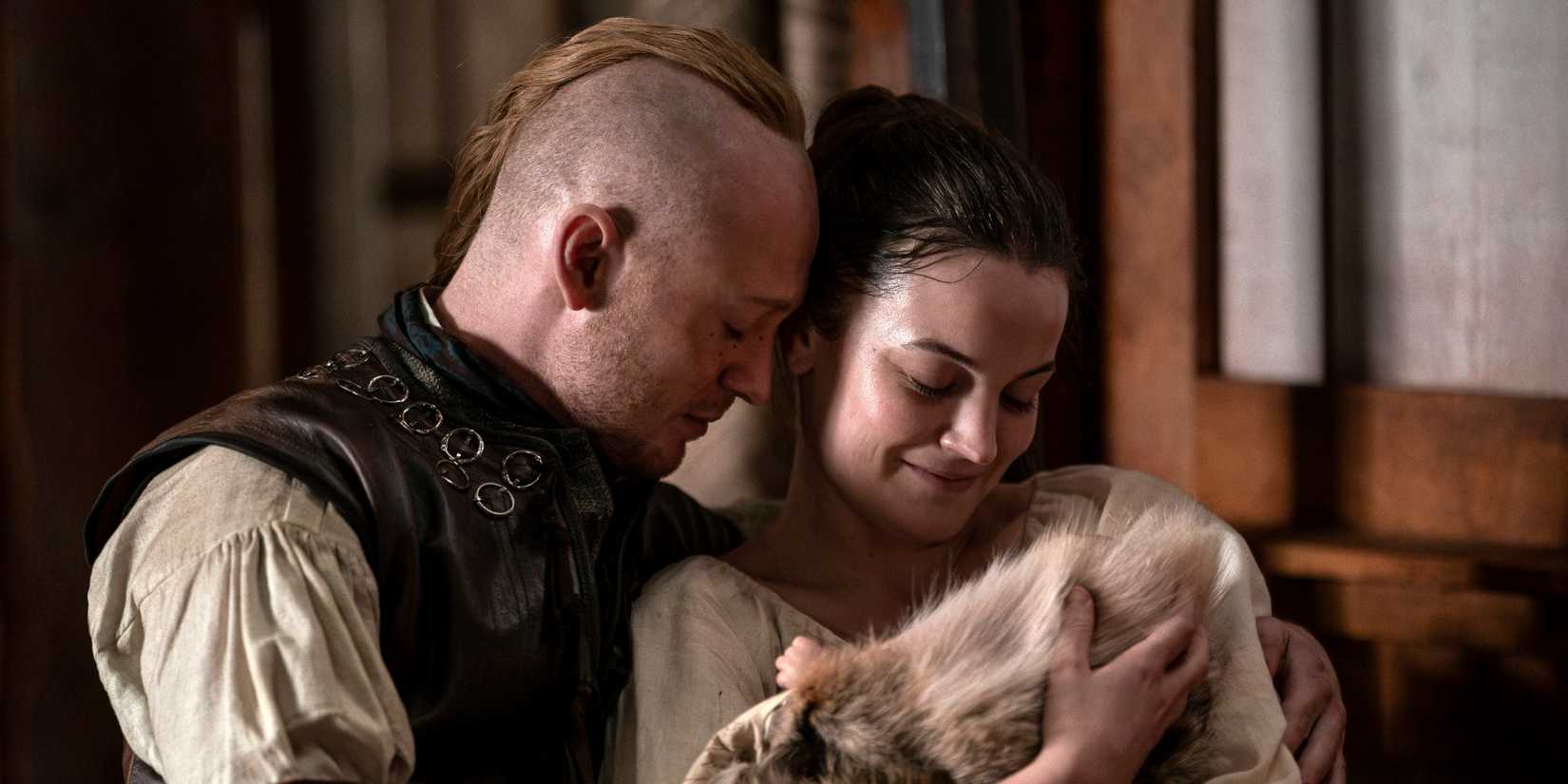 John Bell as Ian standing with Izzy Meikle-Small as Rachel as they hold their newborn in Outlander Season 8