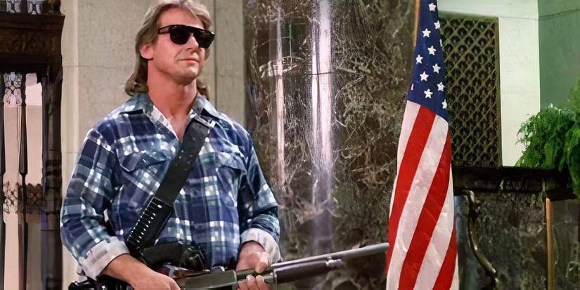 Roddy Piper with a shotgun wearing sunglasses standing next to an American flag in They Live.