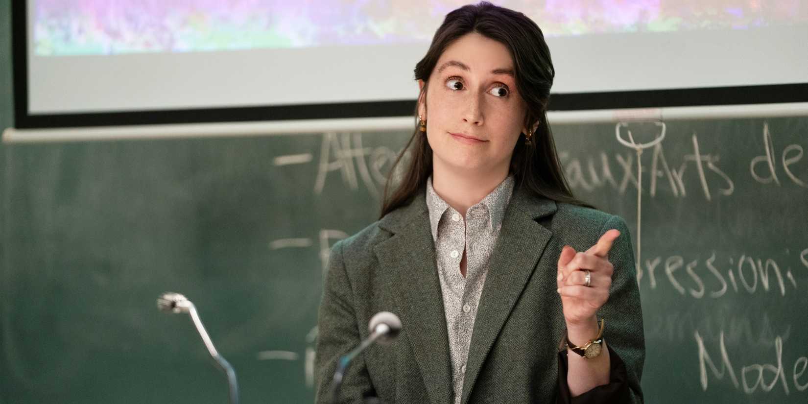 Katie at a lectern in a classroom, pointing at someone.