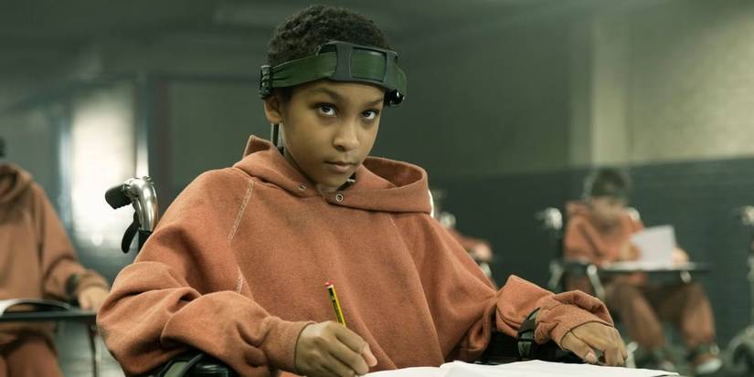 Sennia Nanua as Melanie in a wheelchair with a desk, writes something on paper in The Girl with All the Gifts.