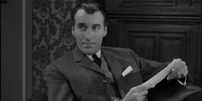 Christopher Lee as Sherlock Holmes sitting and holding a paper in Sherlock Holmes and the Deadly Necklace