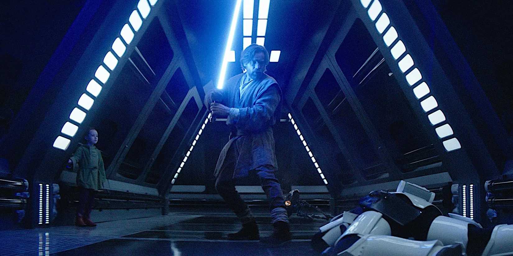 Obi-Wan Kenobi wields his lightsaber in a dark hallway in front of a fallen Stormtrooper as young Leia Organa watches