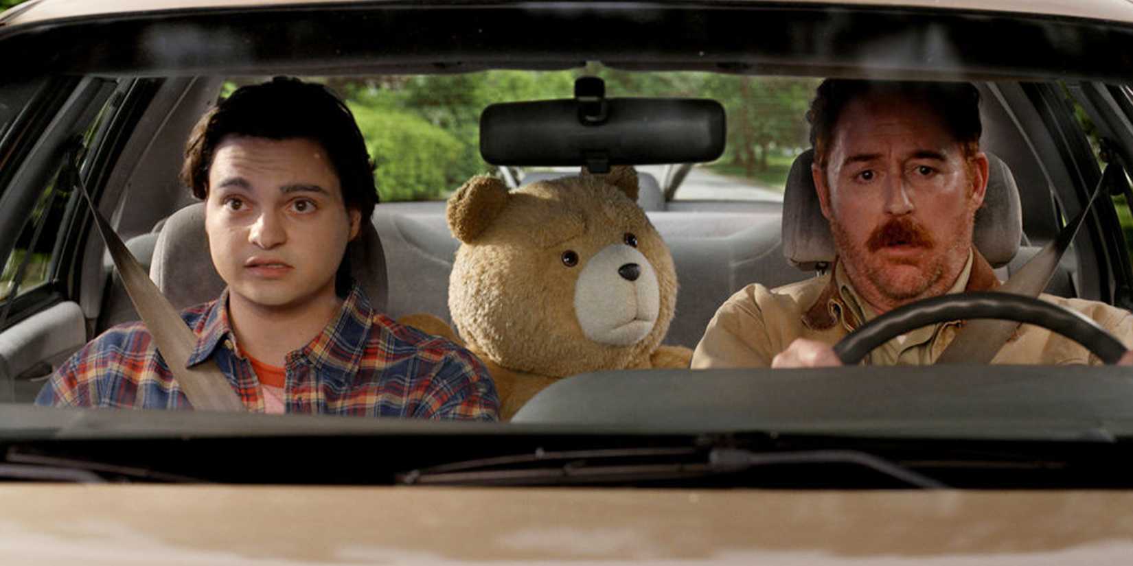 John and Matty are in the front seat of a car, with Ted in the backseat looking at Matty.