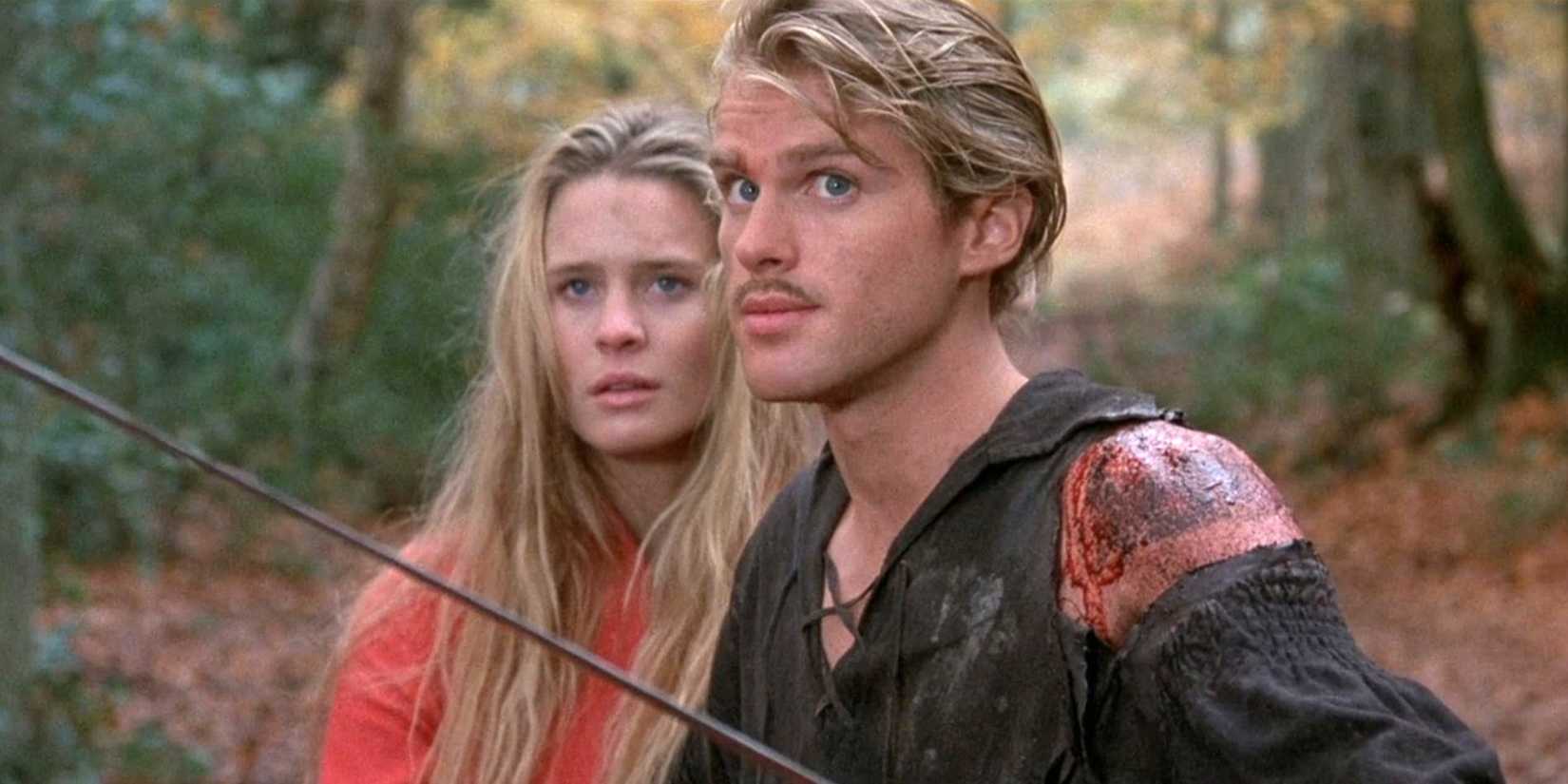 Westley with a wounded shoulder stands on guard with his sword while Buttercup stands behind him in The Princess Bride