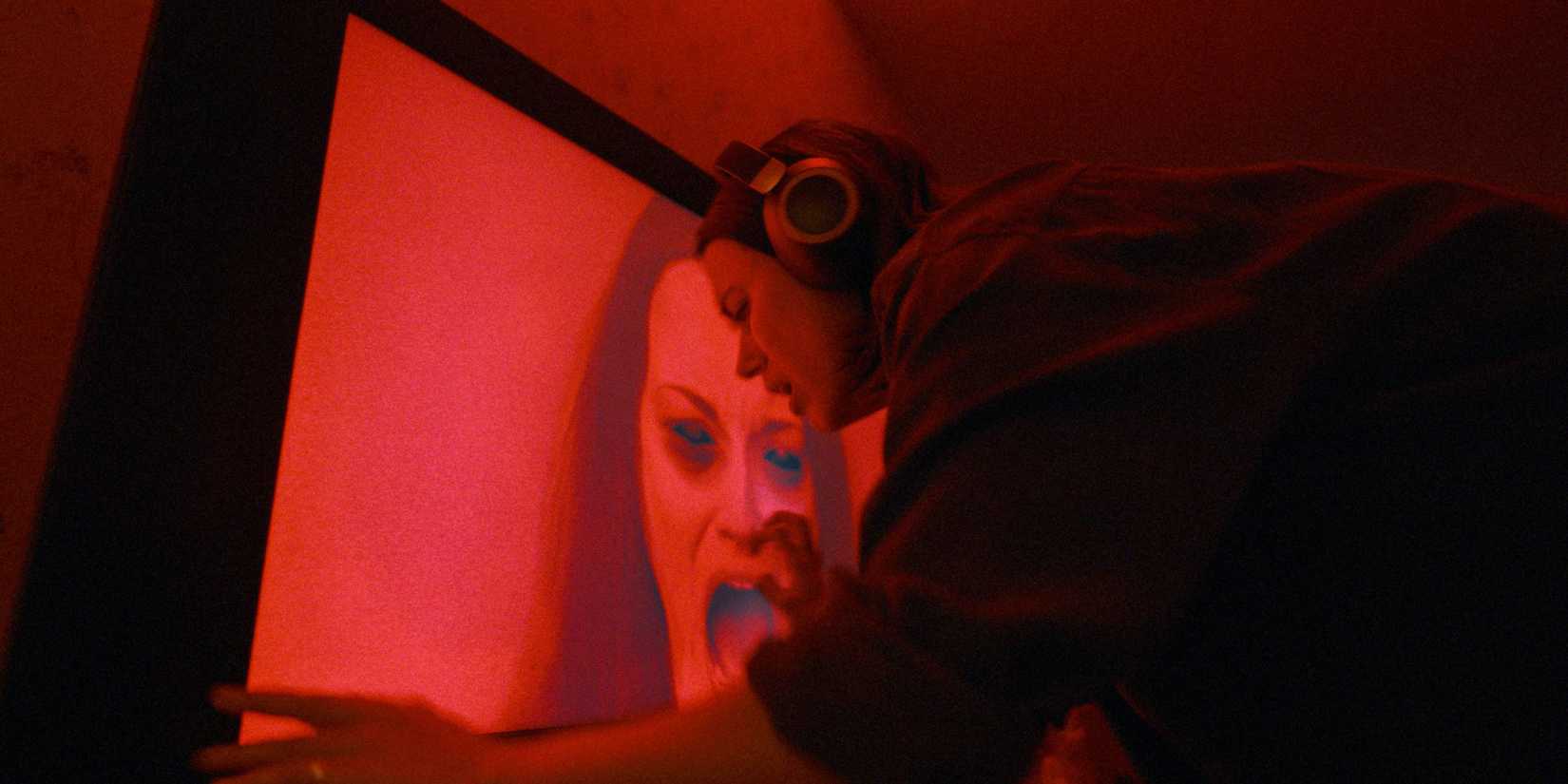 Nina Kiri with headphones on, close to a monitor with a screaming woman, in Undertone
