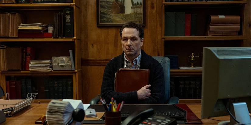 A man sitting behind a desk clutching a binder in Widow's Bay.