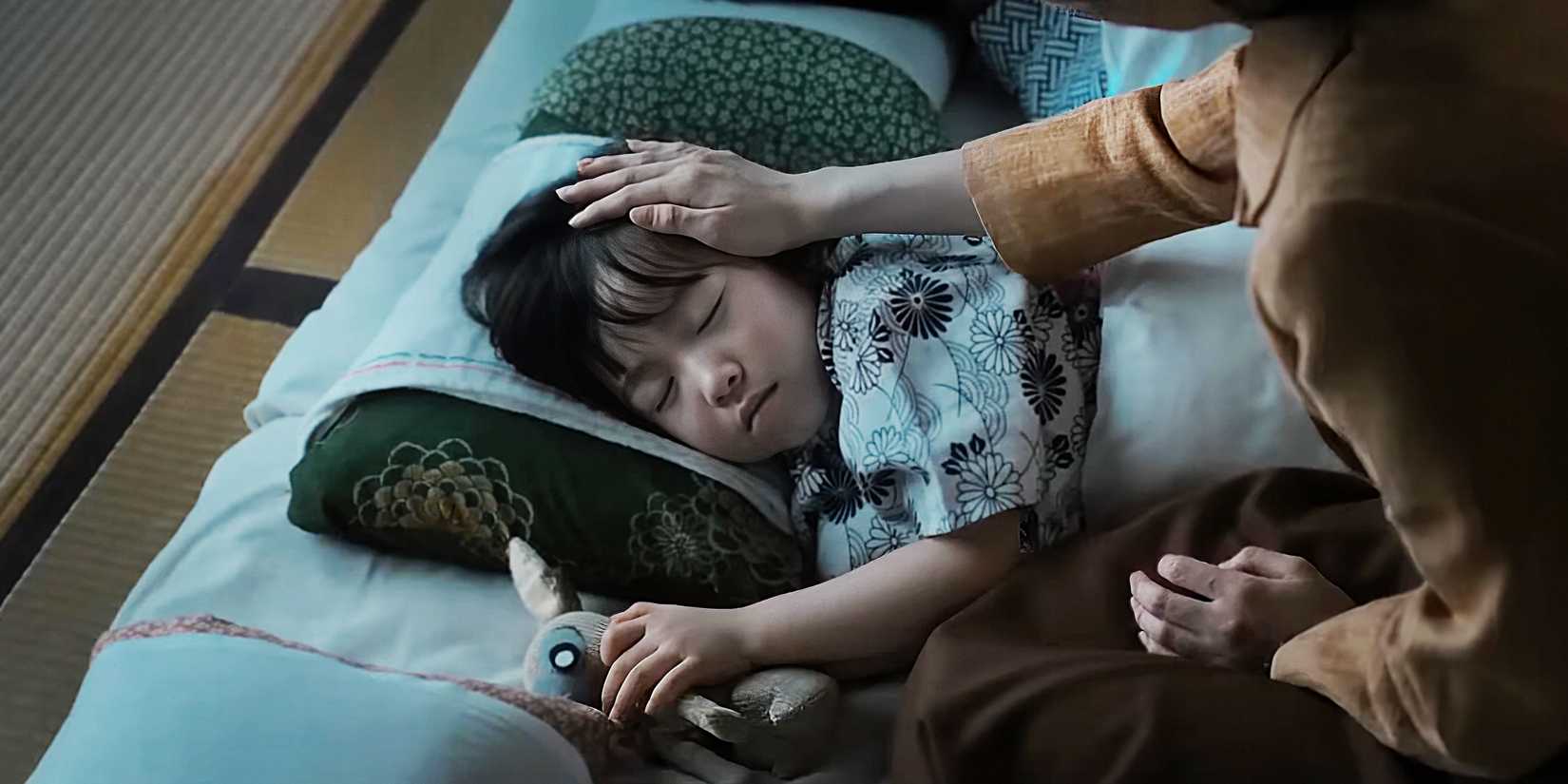 A woman brushes a sleeping little girl's hair back.