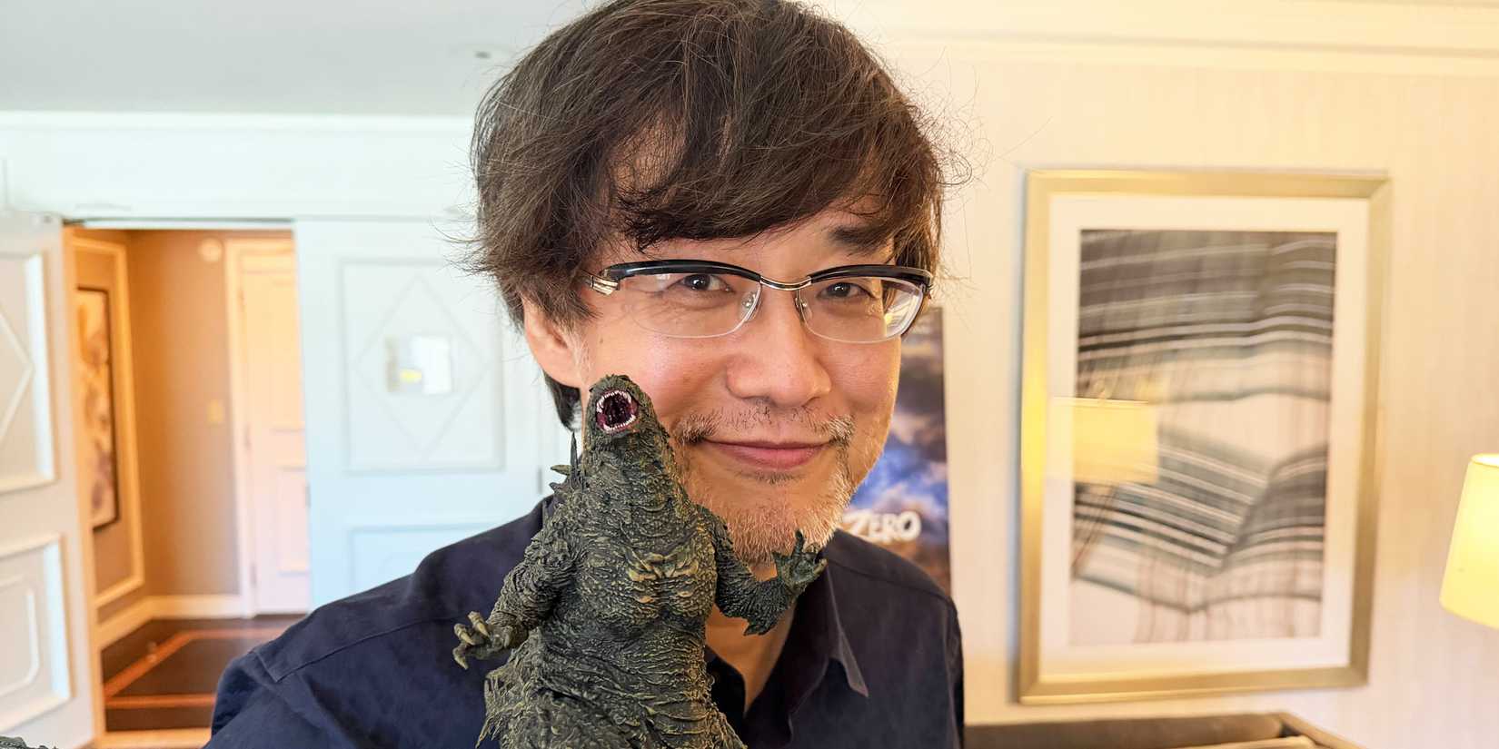 Godzilla Minus Zero writer and director Takashi Yamazaki holds up a Godzilla figure and smiles.
