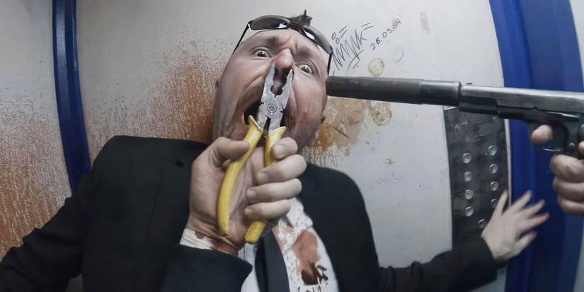 A man in a suit and tie in an elevator with a gun pointed at his head and pliers on his nose in Hardcore Henry.