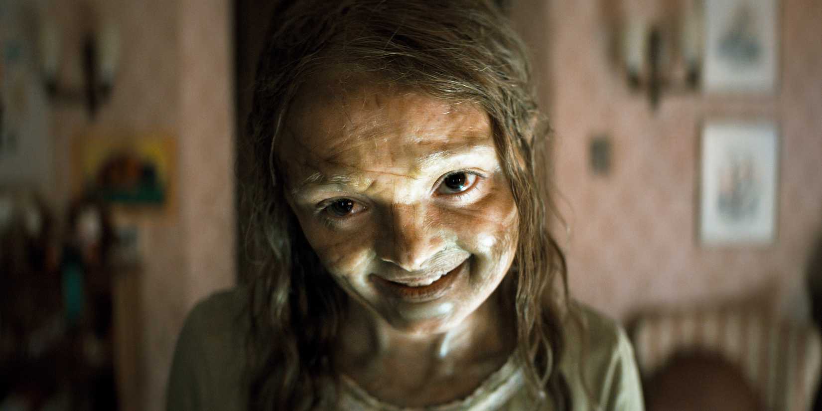 A possessed Katie tilts her head and smiles eerily.