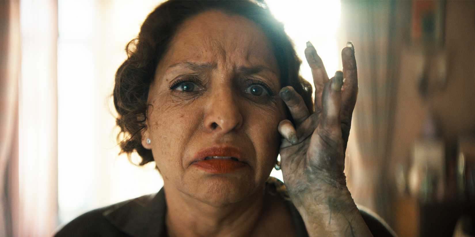A decaying hand caresses the side of Carmen's face as she looks on in horror.