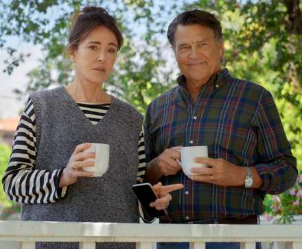 Christa Miller as Liz standing on the balcony with Ted McGinley as Derek in Shrinking Season 3