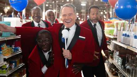 A group of men in red suits singing in a store aisle, led by Hal.