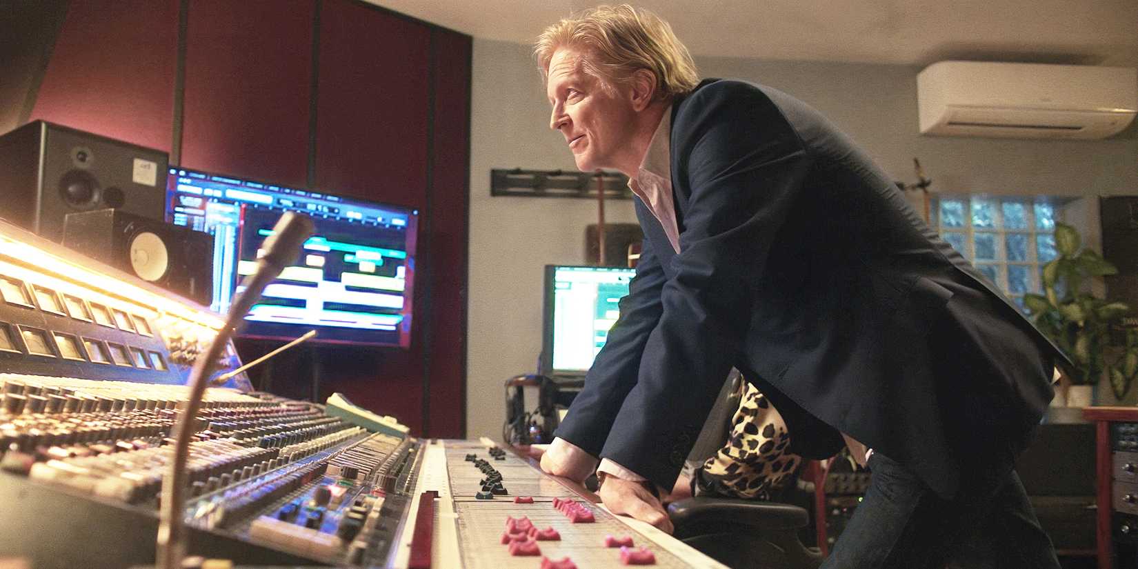 Jake leans over a mixing desk in a studio.