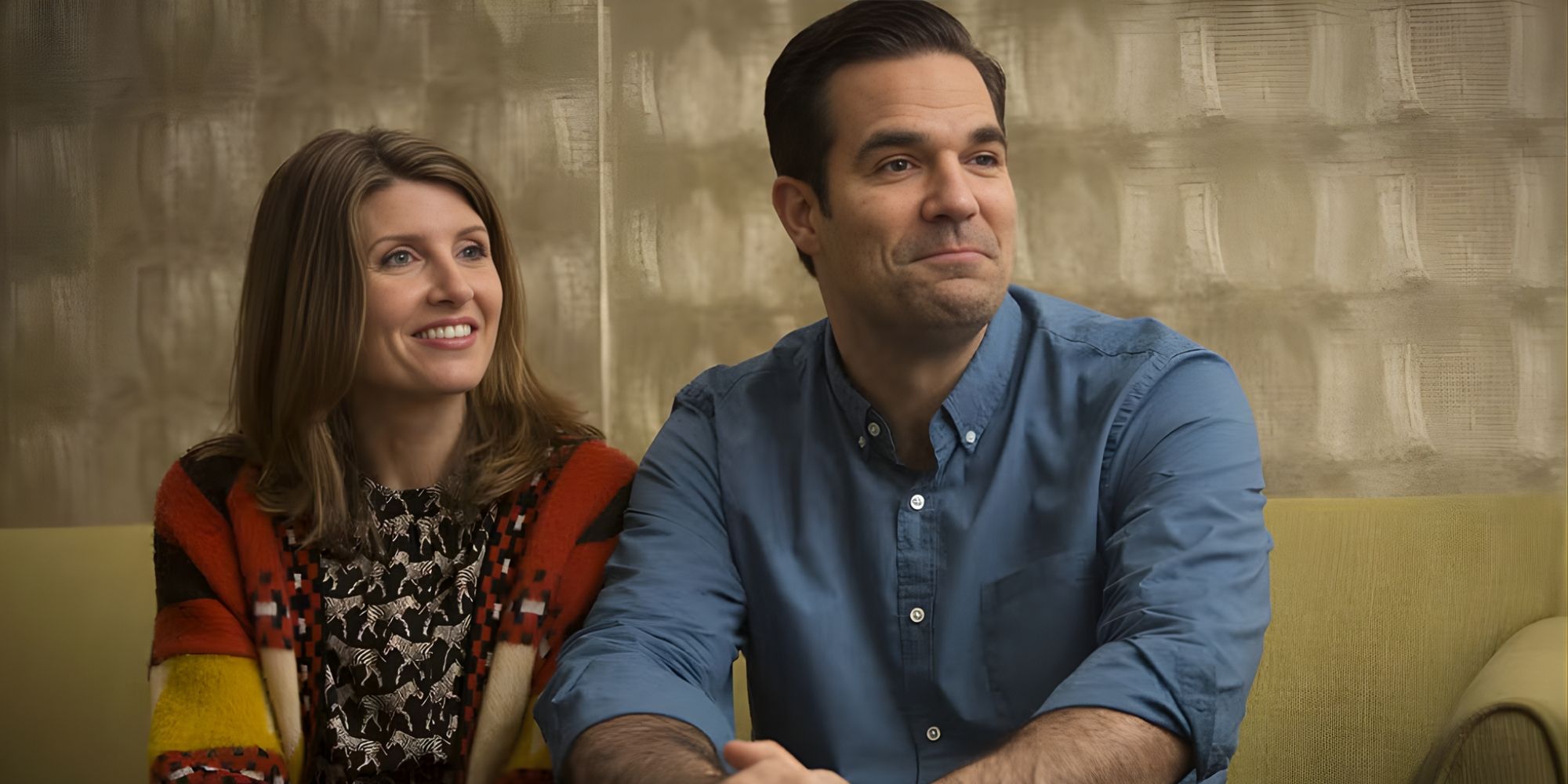 Sharon (Sharon Horgan) and Rob (Rob Delaney) sitting on a couch, looking to the right, in Catastrophe.