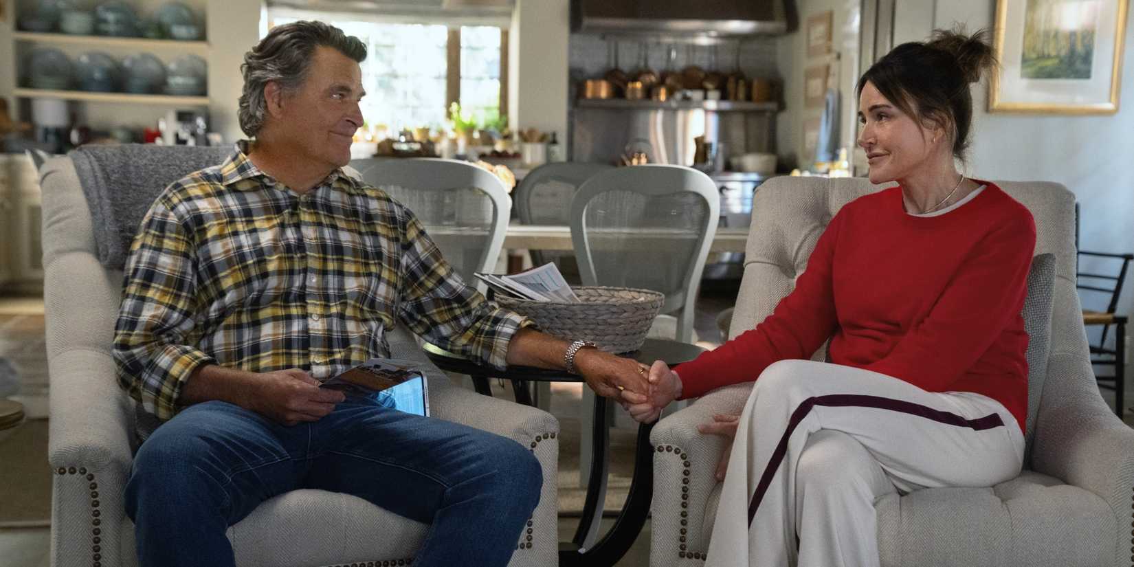 Christa Miller as Liz sitting in a chair next to Ted McGinley as Derek as they hold hands in Shrinking Season 3