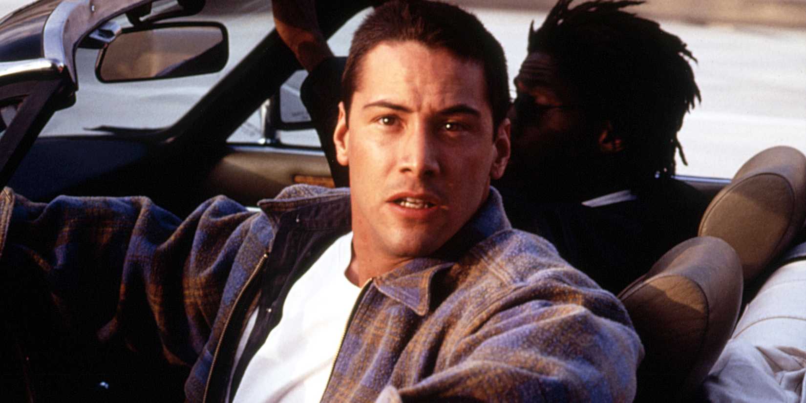 Keanu Reeves at the wheel of a car facing his right in Speed