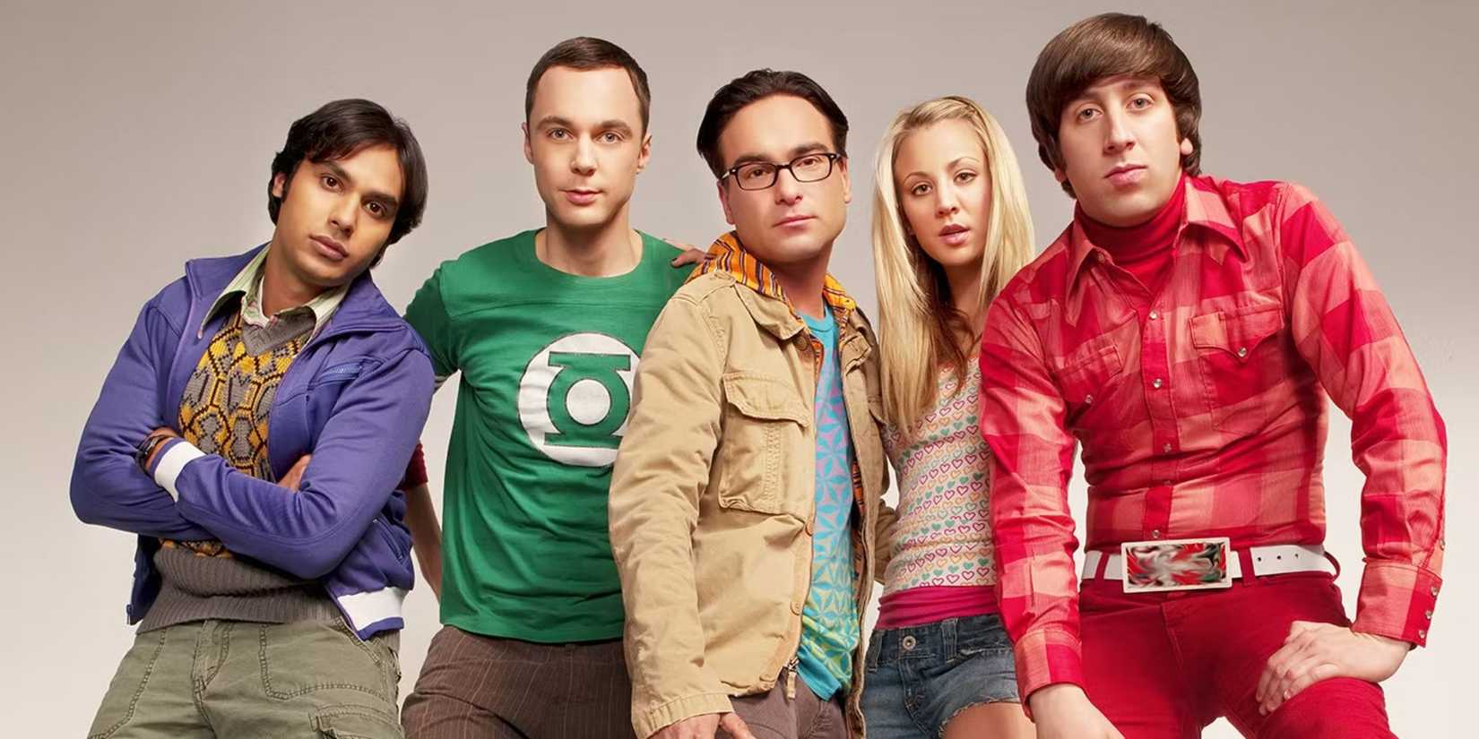 The cast of The Big Bang Theory pose for a promo photo and look at the camera with a plain backdrop.