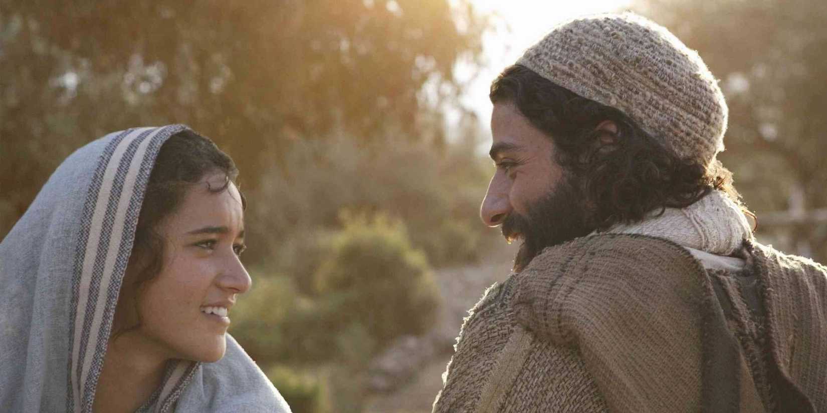 Keisha Castle-Hughes as Mary and Oscar Isaac as Joseph smile at each other outside by trees in The Nativity Story