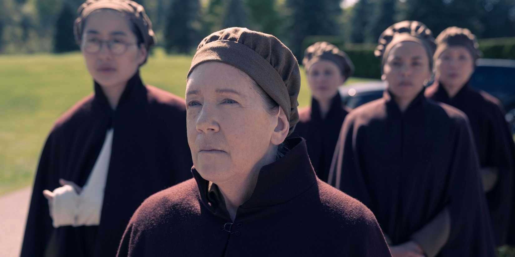 Ann Dowd as Aunt Lydia wearing a coat and cap with Mabel Li as Aunt Vidala behind her in The Testaments