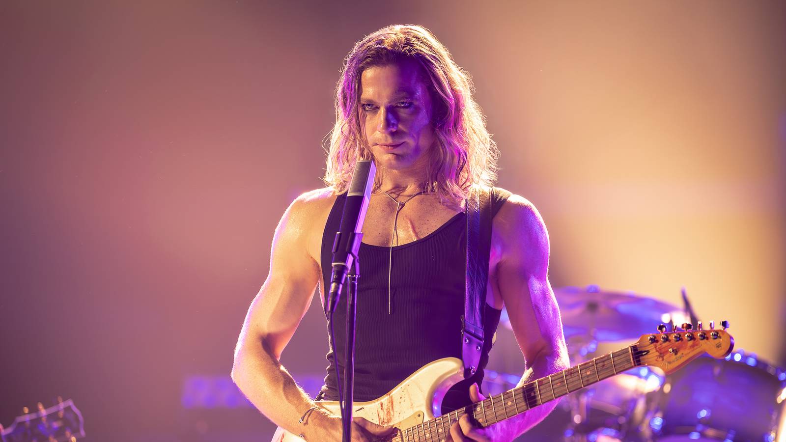 Sam Reid holding a guitar and standing in front of a microphone in The Vampire Lestat