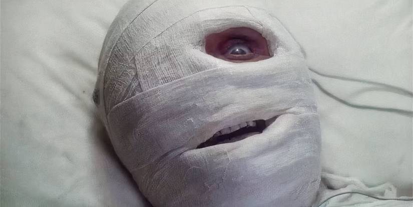 A man with his face covered in bandages with one eye wide open in Dead & Buried
