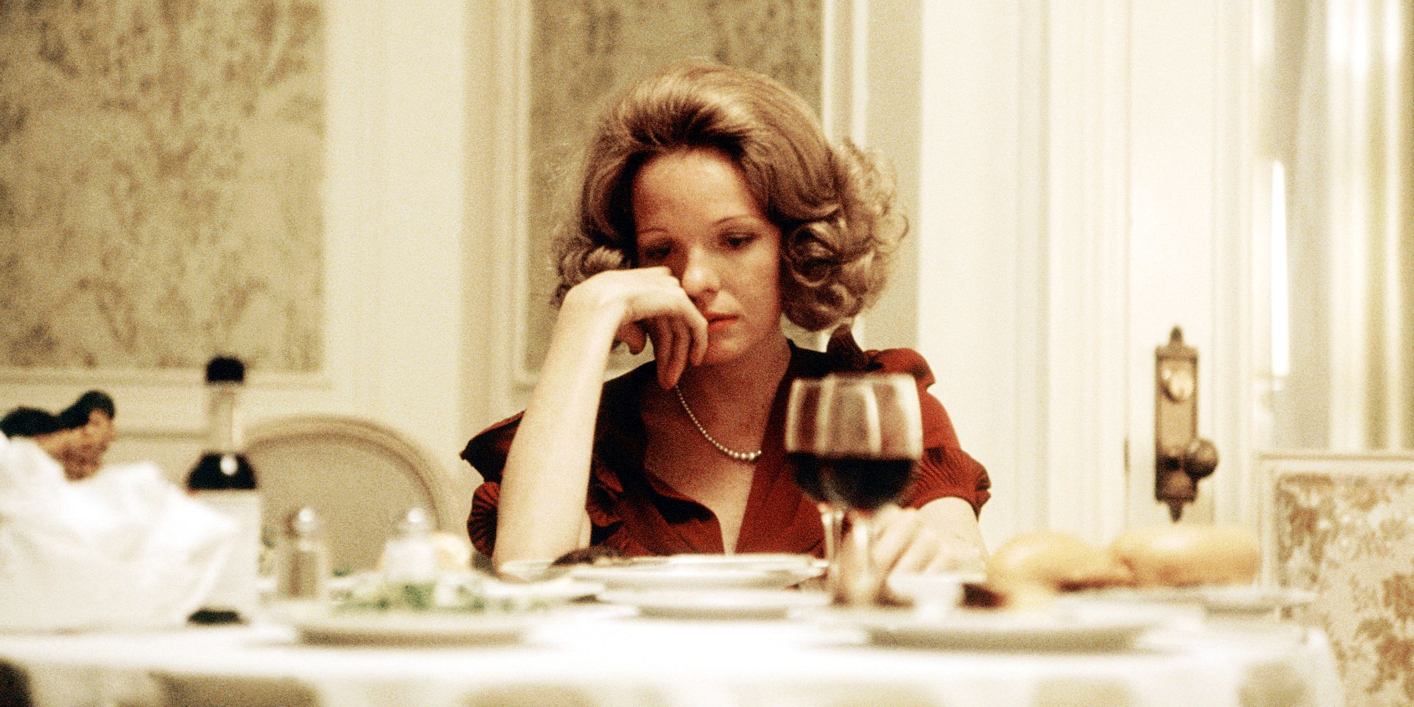 Diane Keaton looking sad at a table with a glass of wine in The Godfather