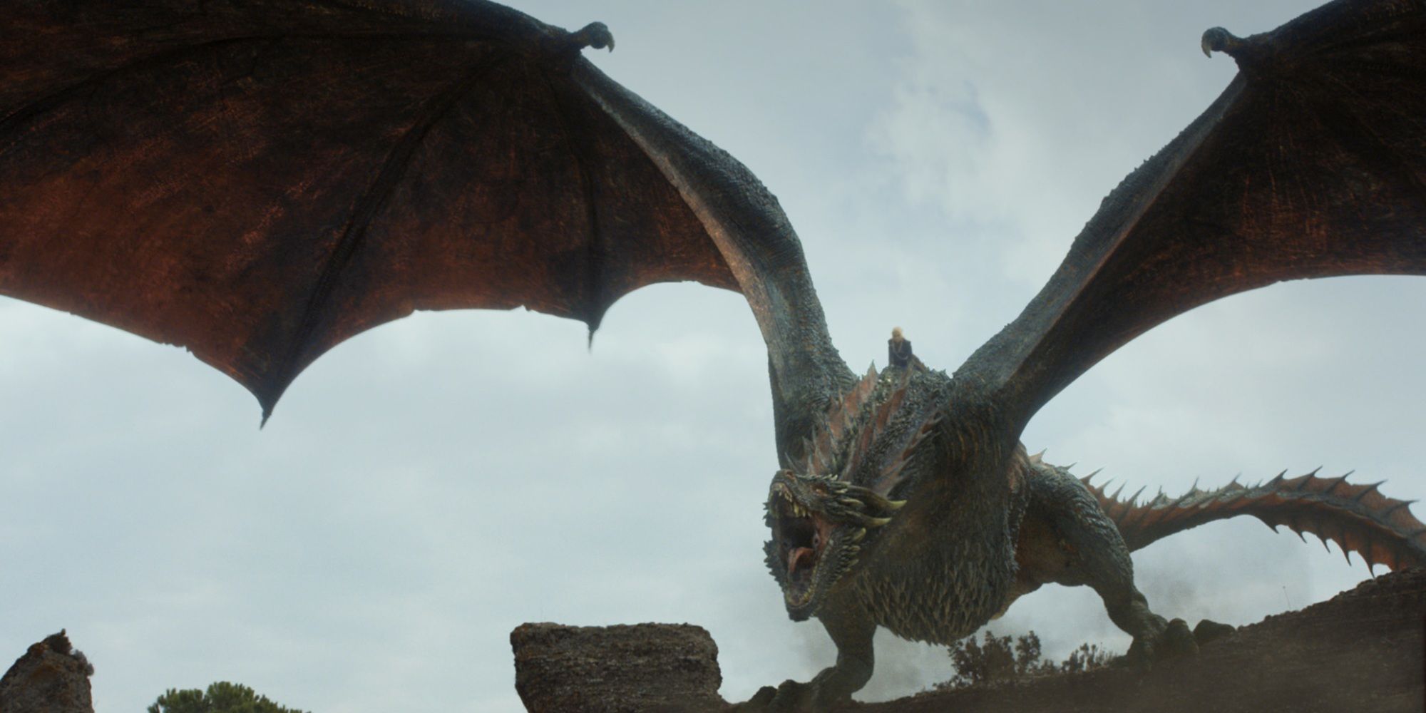 Daenerys Targaryen (Emilia Clark) sitting on the back of her dragon Drogon who is perched on a stone wall screeching with his wings flaired in Game of Thrones Season 7.