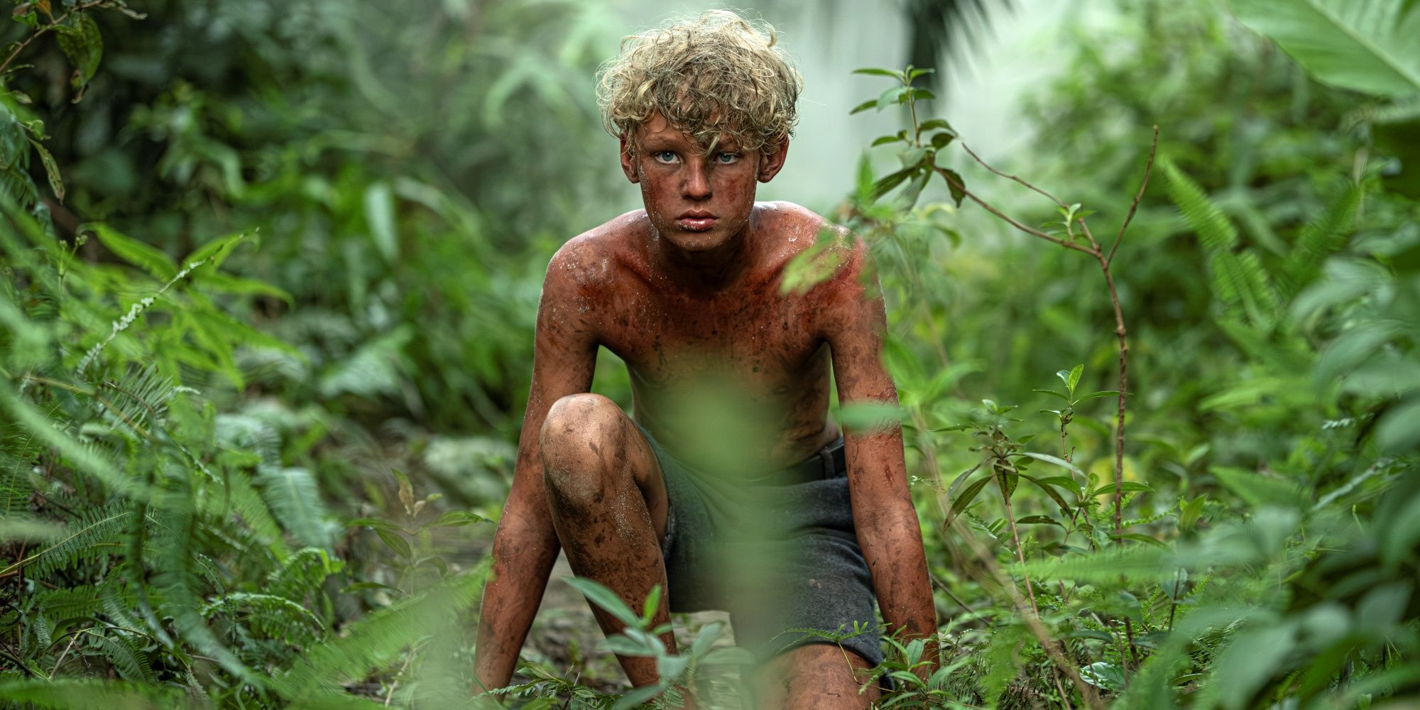 Lox Pratt as Jack crouched down in the jungle and covered in dirt in Lord of the Flies
