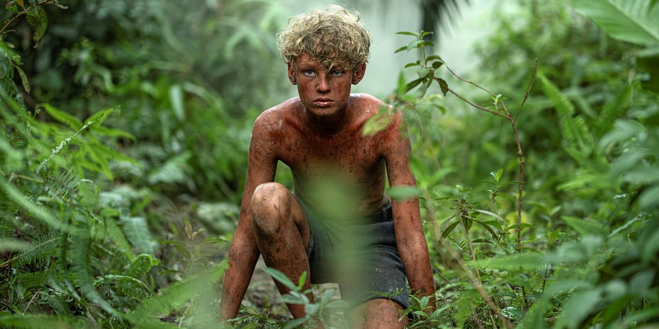 Lox Pratt as Jack crouched down in the jungle and covered in dirt in Lord of the Flies