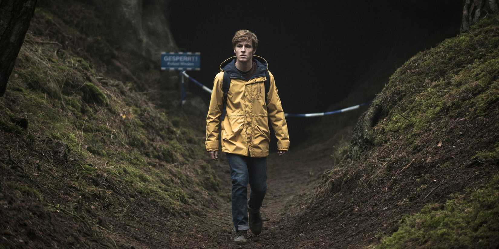 Louis Hofmann in a yellow jacket walking in a cavern in the woods in Dark (2017)