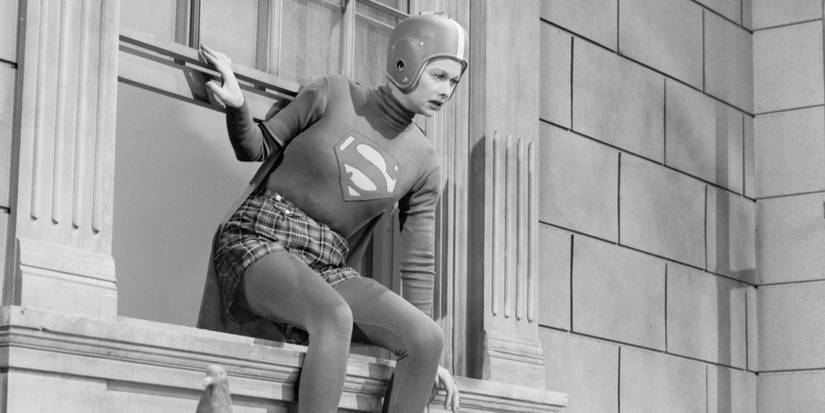 Lucy (Lucille Ball) sitting on a window ledge wearing a Superman costume and a helmet.