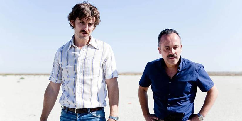 Raúl Arévalo and Javier Gutiérrez standing in a desolate area and talking to someone off screen in Marshland