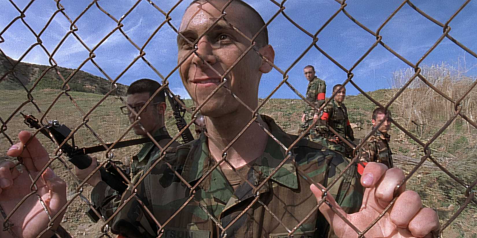 Justin Berfield as Reese dressed in camo fatigues and gripping a chain link fence in