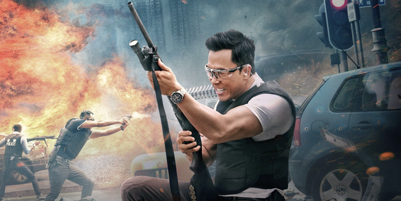 A man holds a rifle while an explosion happens behind him.