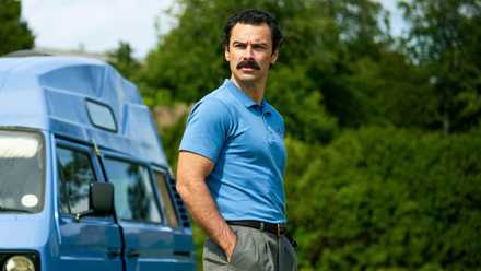 Aidan Turner with his hands in his pockets outside a blue van in 'Rivals'