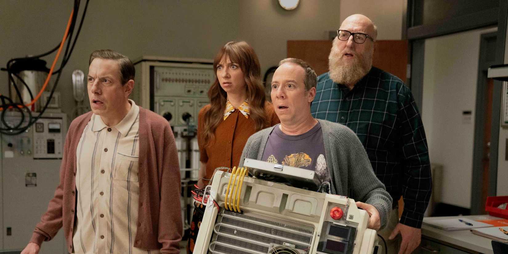 The cast of Stuart Fails to Save the Universe gathered in an office with a device