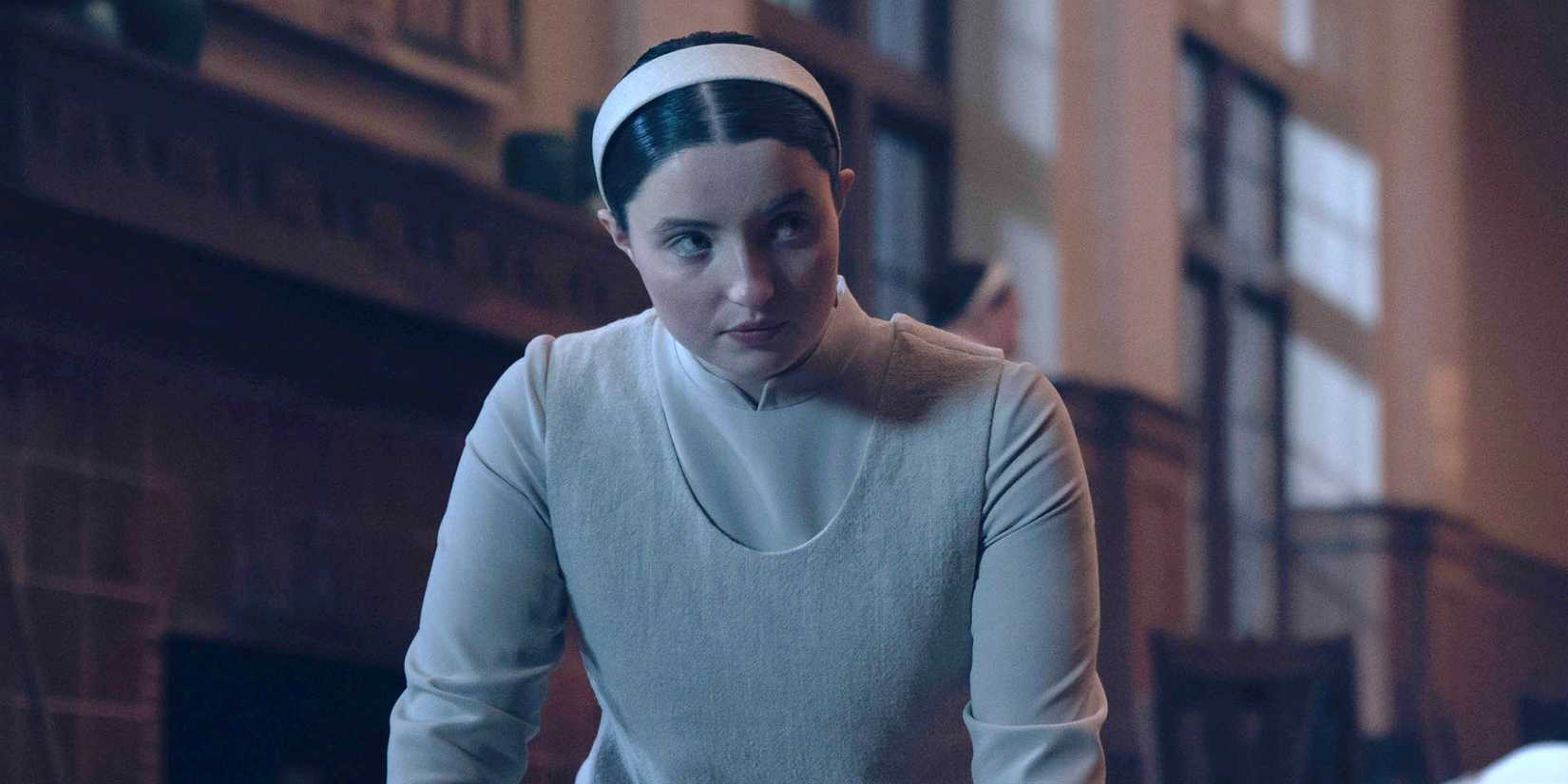 Lucy Halliday as Daisy dressed in all white with a white headband in The Testaments