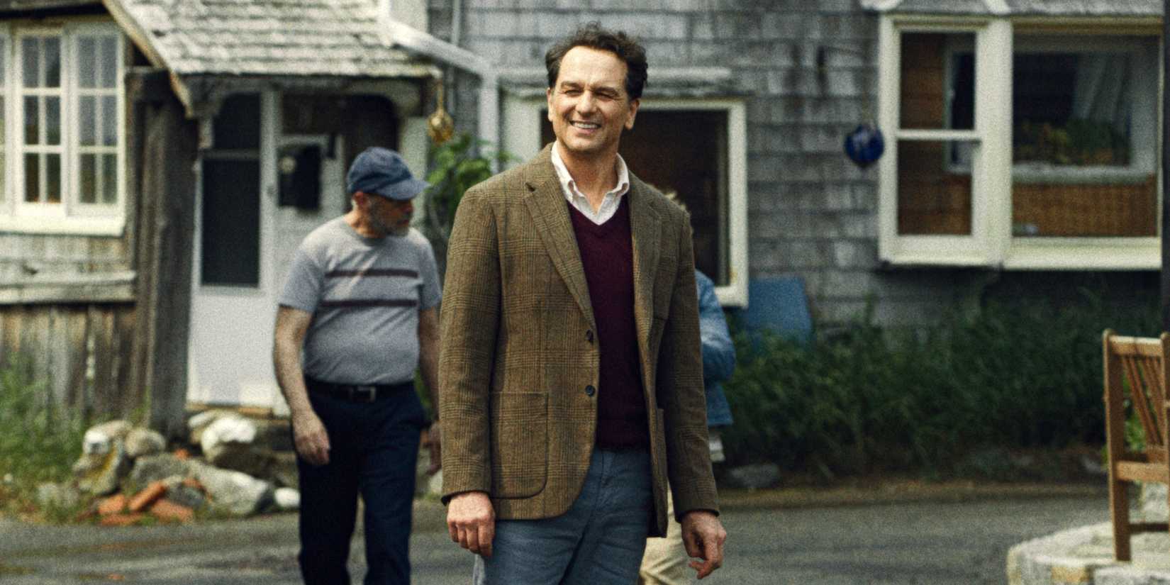 Matthew Rhys as Tom standing outside with a smile in Widow's Bay