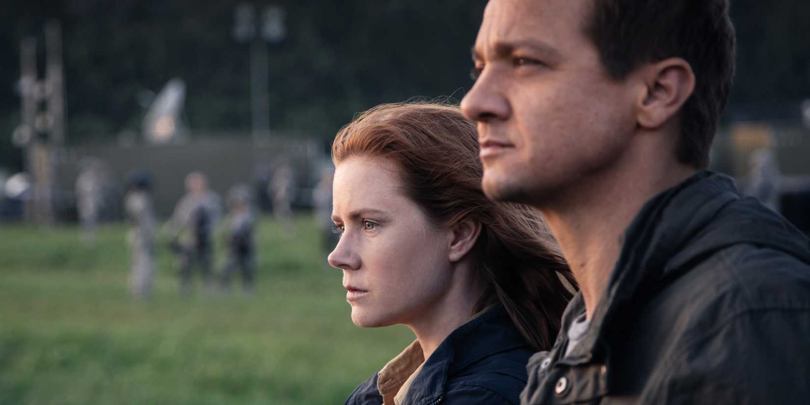 Amy Adams and Jeremy Renner stand side-by-side outdoors and stare ahead in Arrival.