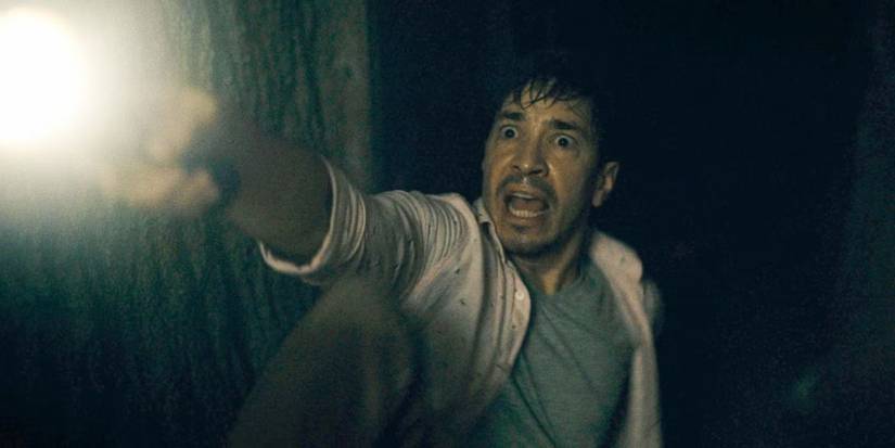 Justin Long pointing a flashlight in the dark and yelling at something off-screen in Barbarian (2022)