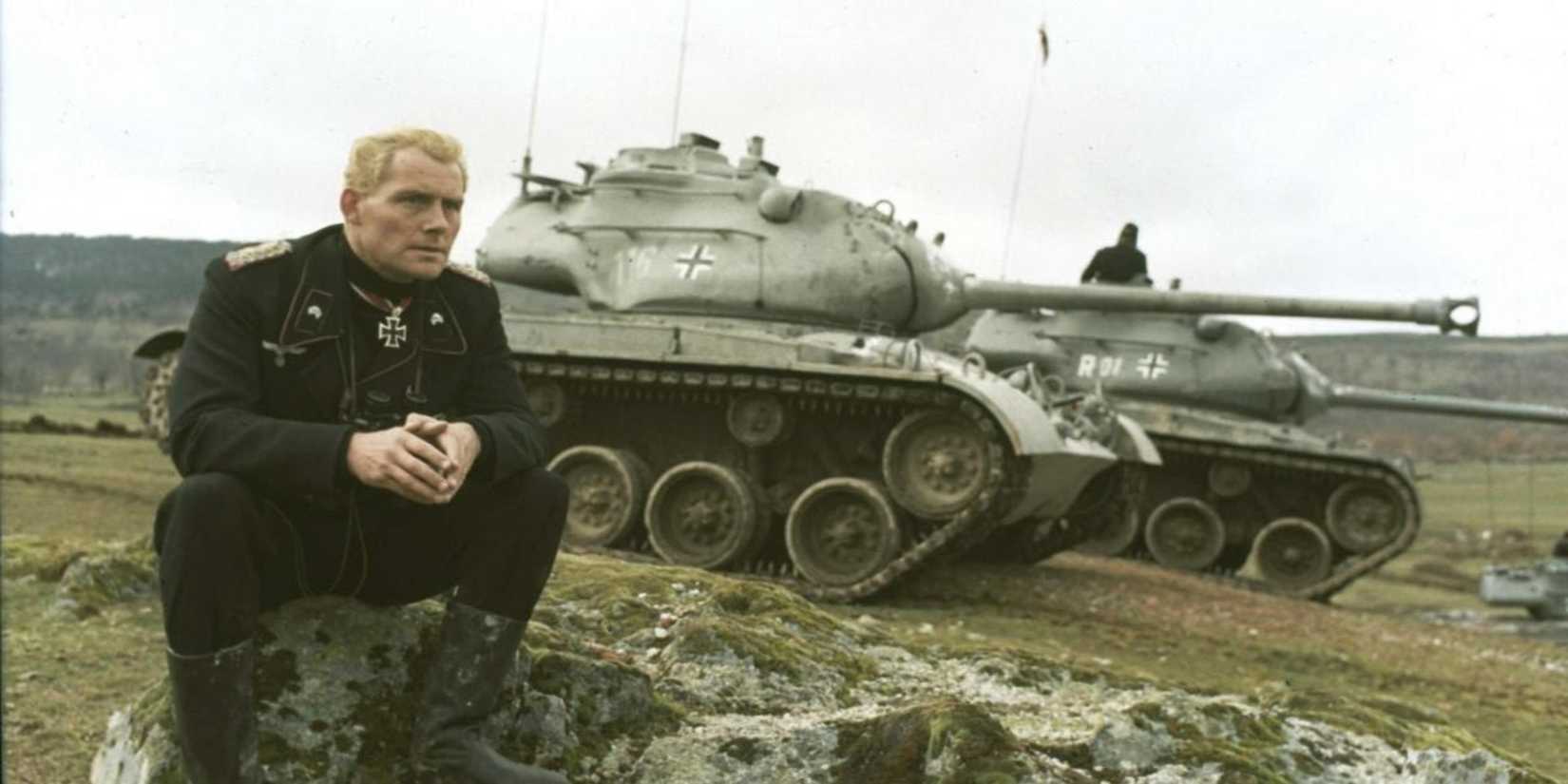 A soldier sitting on a rock with a tank behind him in Battle Of The Bulge
